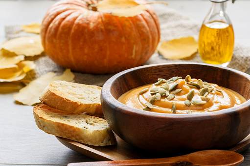 Pumpkin soup in a wooden bowl, with autumn leaves and pumpkin